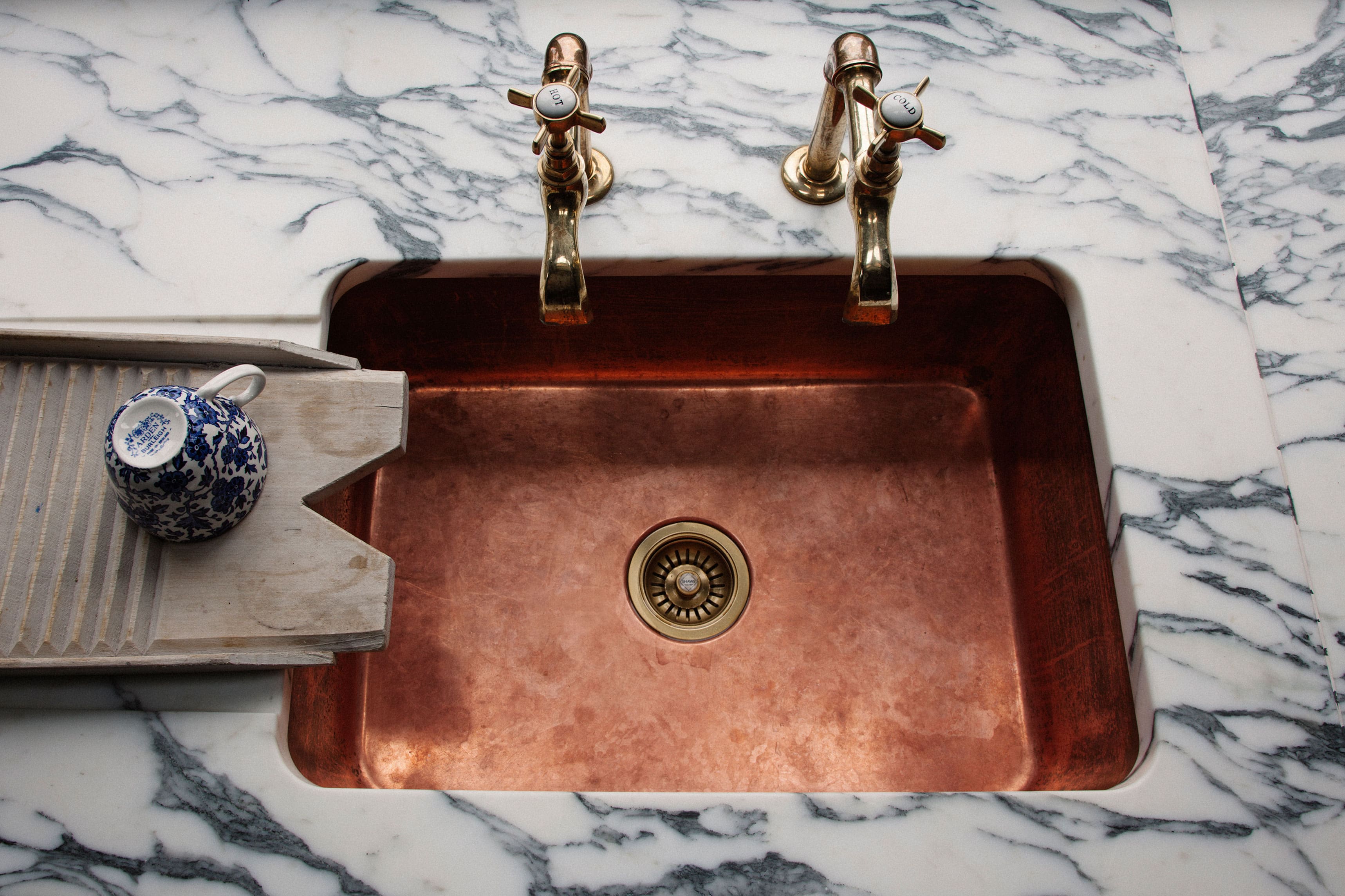  Elegant English-style kitchen with light grey cabinetry, open shelving, and a farmhouse sink, emphasizing the bespoke cabinetry and handcrafted finishes by Plain English.