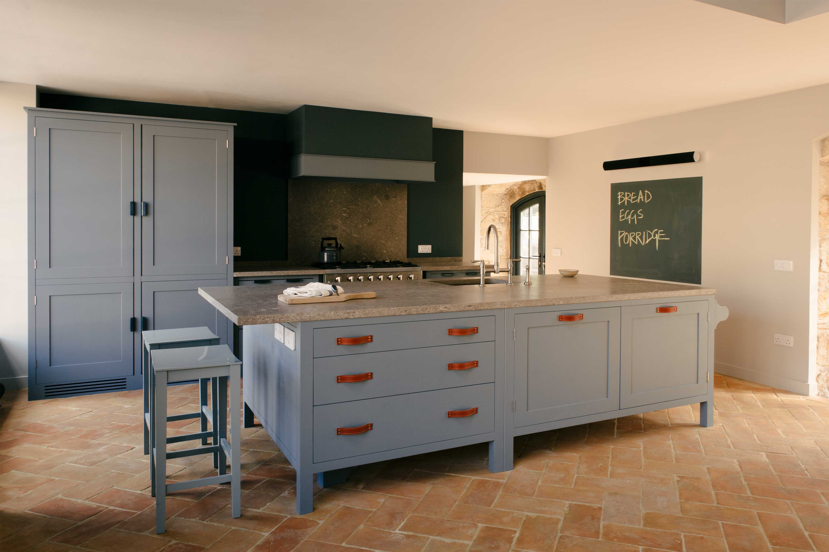  Rustic kitchen with gray cabinetry, a large island with leather handles, a stone countertop, terracotta tile flooring, and chalkboard.
