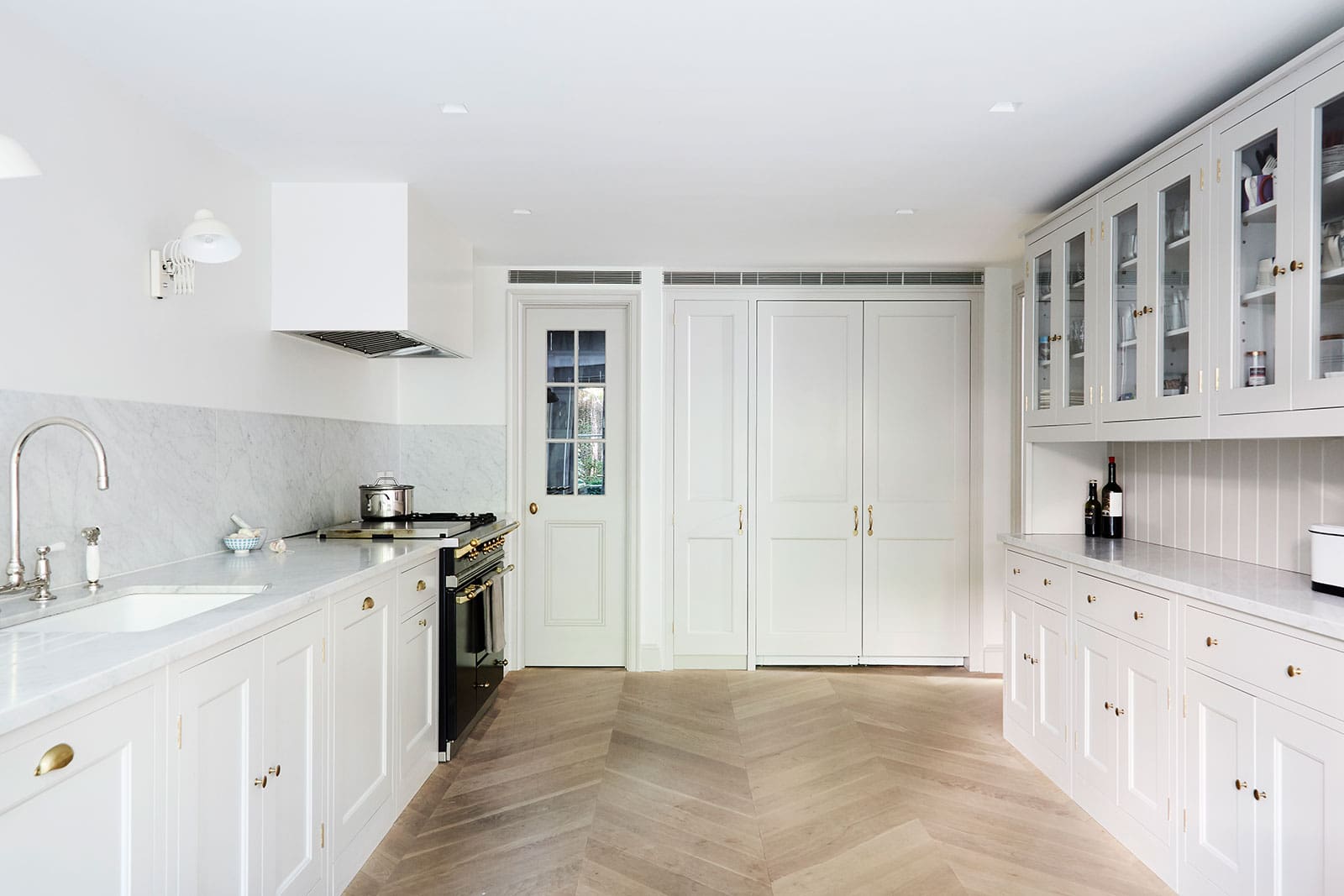  White kitchen with marble backsplash, paneled cabinets, and glass-front storage.