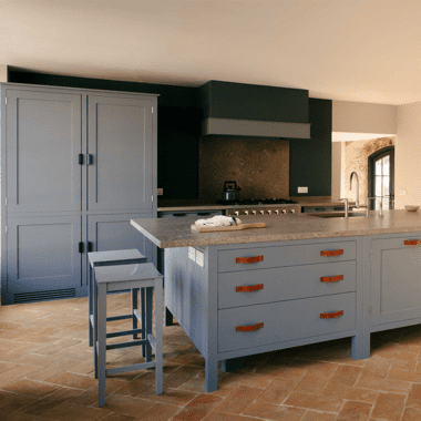 Rustic kitchen with gray cabinetry, a large island with leather handles, a stone countertop, terracotta tile flooring, and chalkboard.