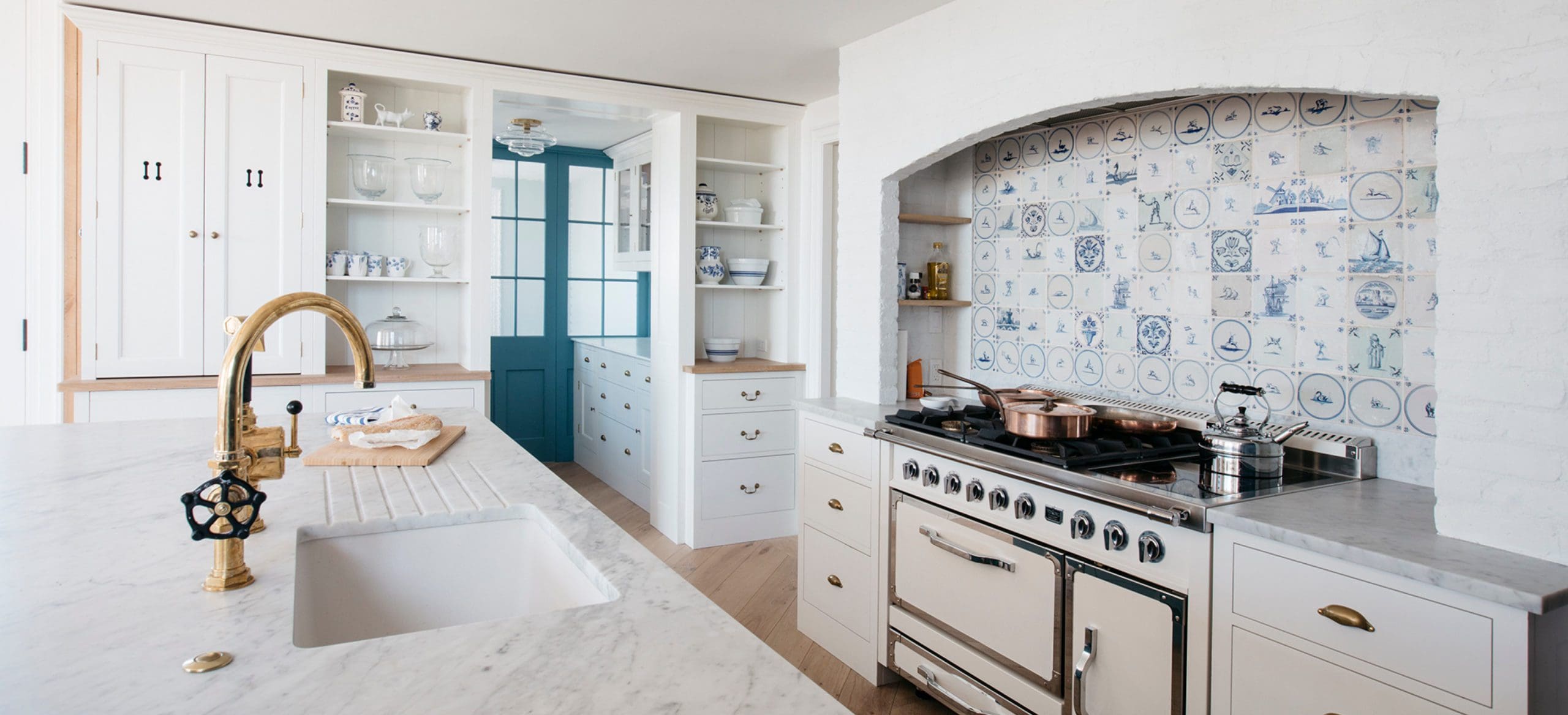  Modern beach house kitchen with antique brass faucet, Delft tile backsplash, marble island, and sculery storage.