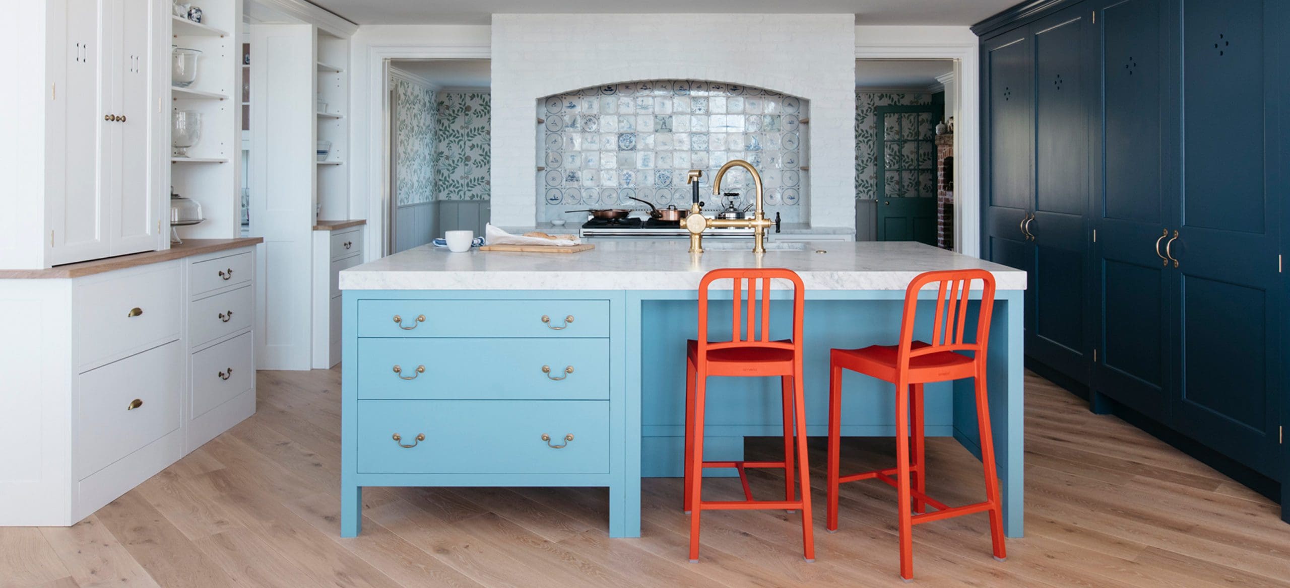  Blue island with brass handles, red chairs and marble countertops in Long Island beach house kitchen.