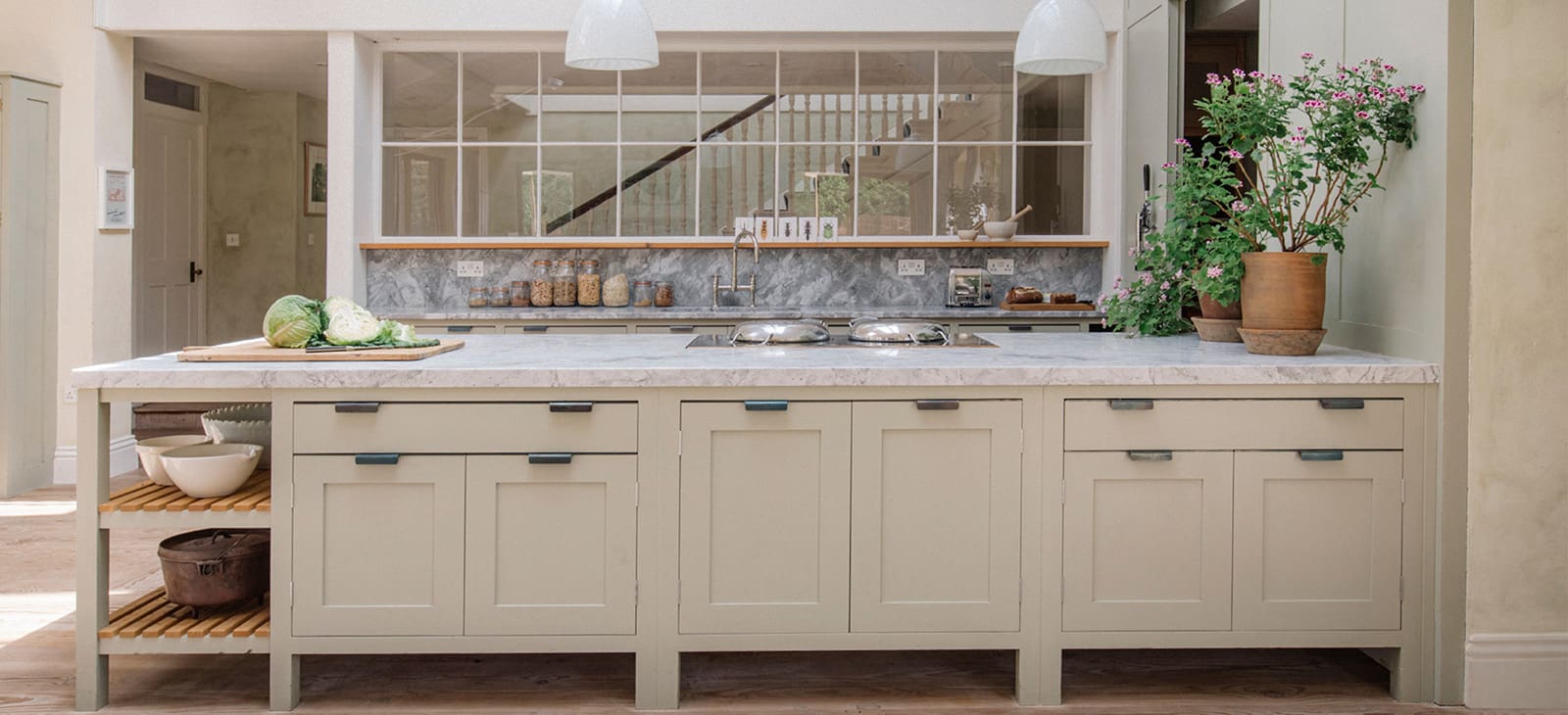  Kitchen island with marble countertop, sage green cabintry, open shelving below ,complented by pendant lights and gray marble backsplash.
