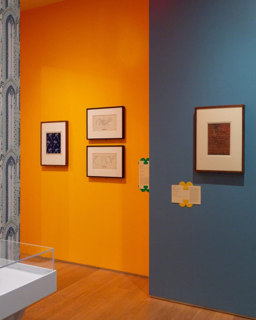The intersection of a blue and orange wall with framed art pieces along both.