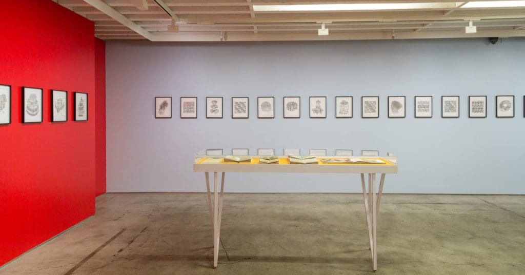 Wooden drawing table with a yellow top covered in books, with simple art hanging on the wall behind it.