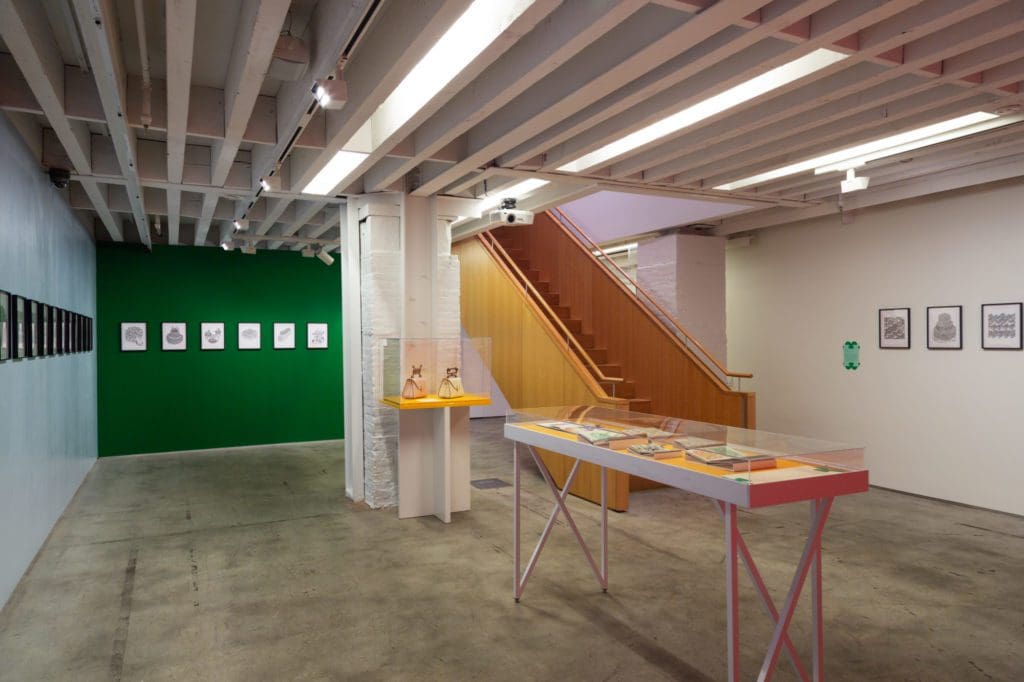 Drawing center with a white and yellow table in the center, wood staircase, and white and green walls.