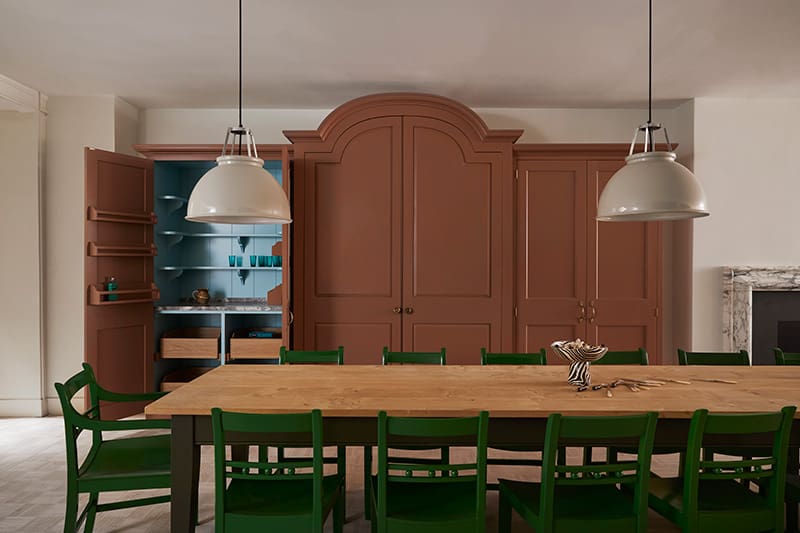 Custom designed larder with brown doors behind a long wooden table.