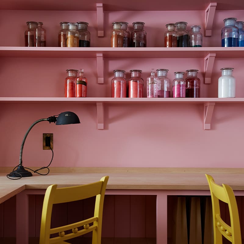 Close up of a wooden desk and chairs with custom open pink shelving overhead.