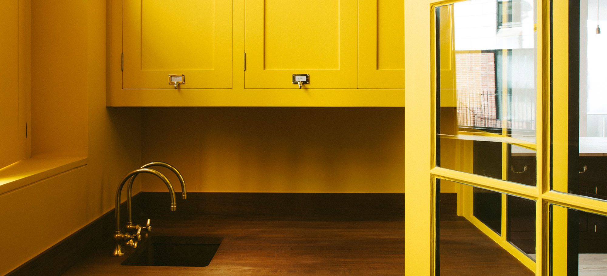 Close up of a sink set in wood countertops, surrounded by bright yellow cabinets in a custom designed scullery. 