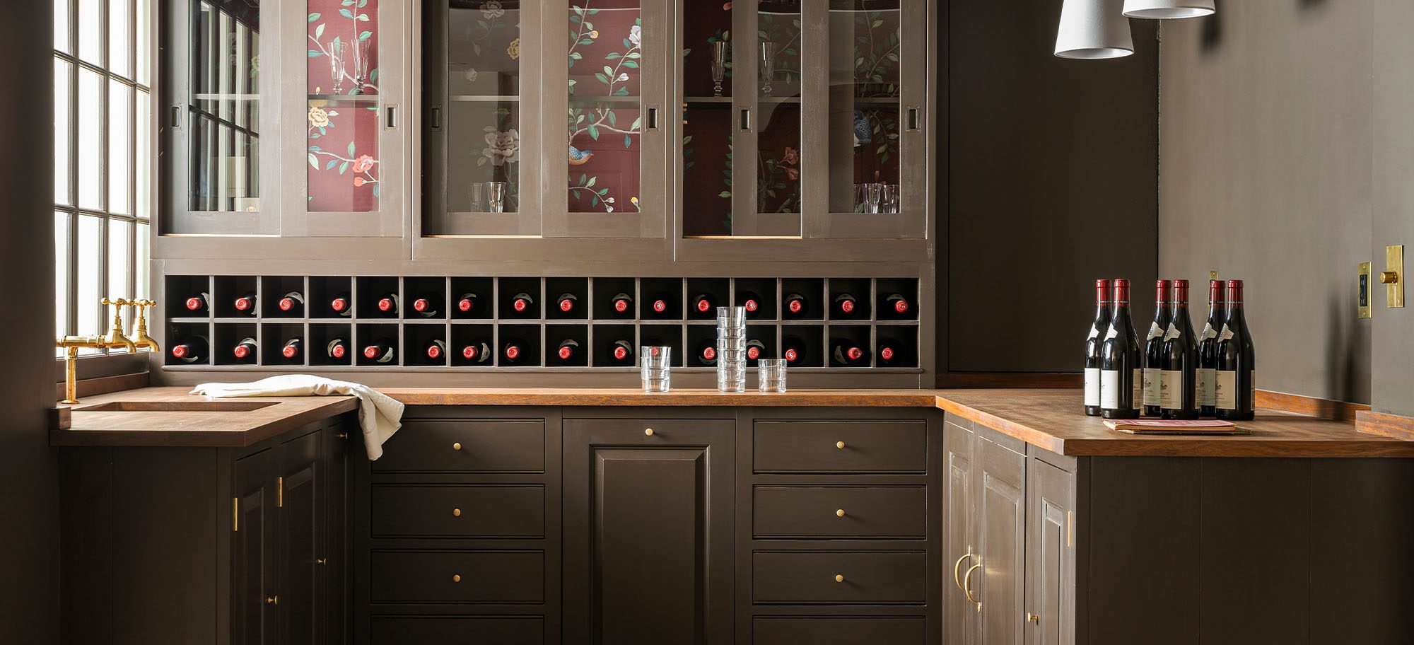 Bespoke wine room, featuring bottles in a cubby-style storage section and custom glass-fronted cabinets. 