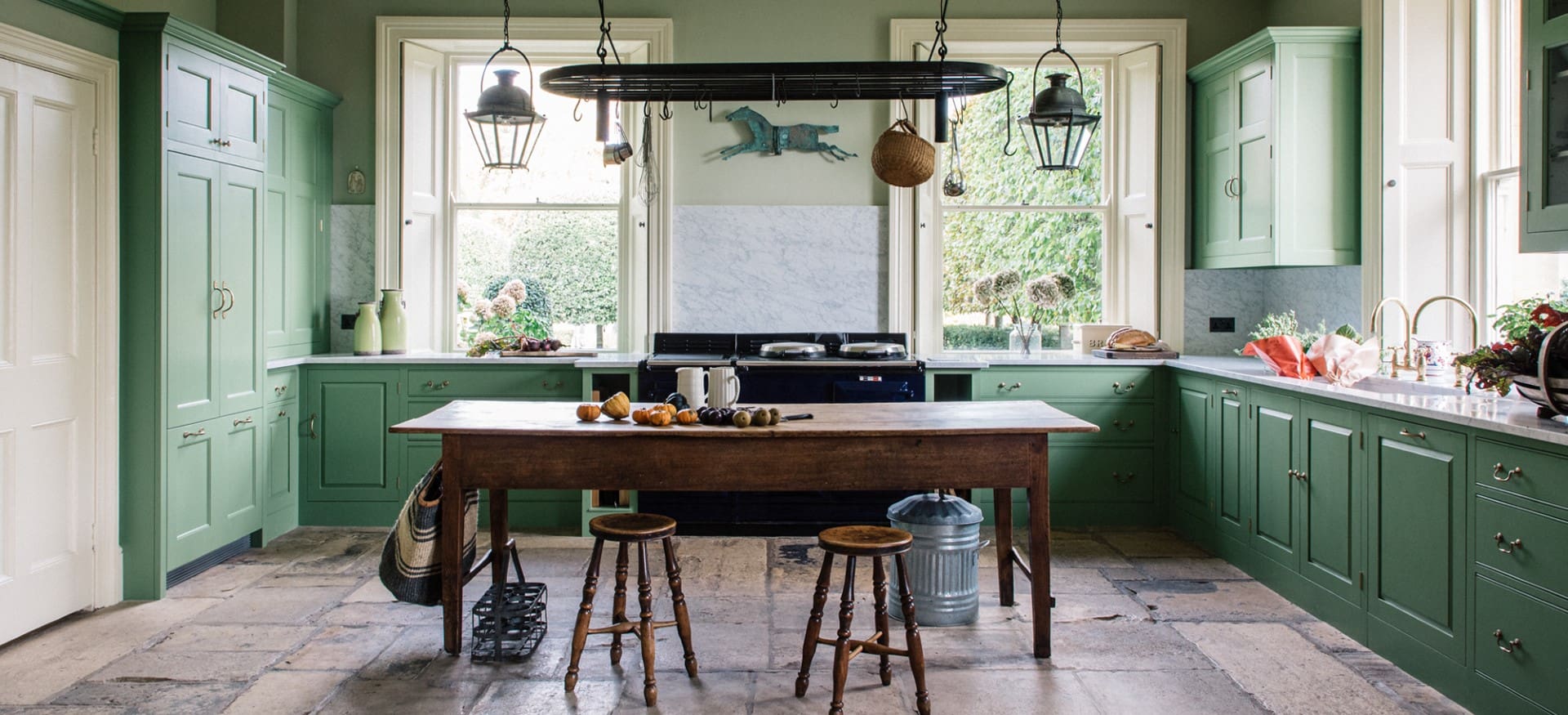  Farmhouse kitchen with green-painted cabinetry, marble backsplash, dark rustic wood table, and lantern lighting.