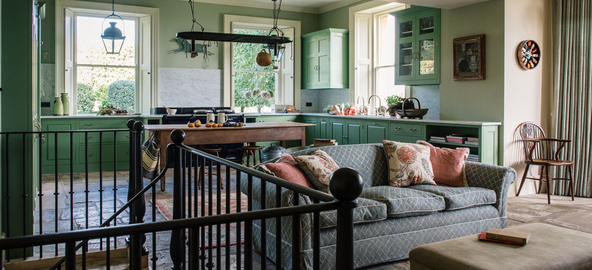  Traditional kitchen with green-painted cabinetry, marble backsplash, rustic wood table, and cozy sitting area.