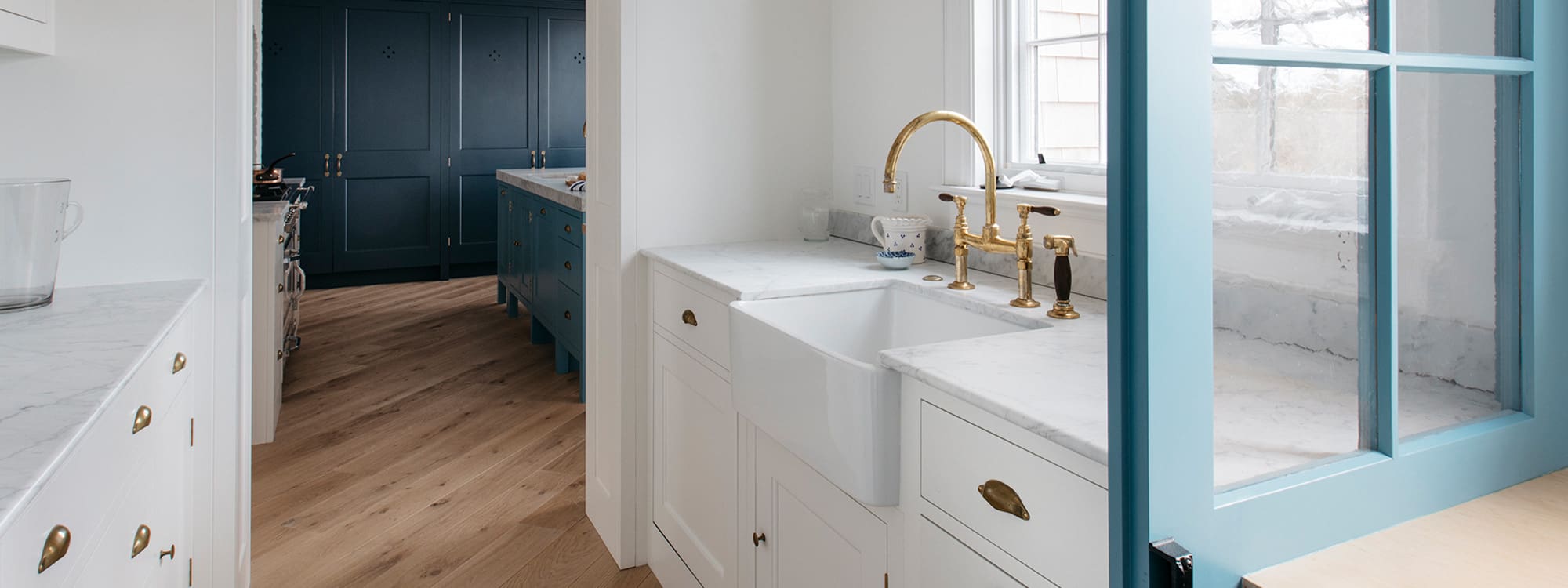 Bespoke kitchen pantry design, featuring a farmhouse sink over custom white cabinets and light blue windowed doors.