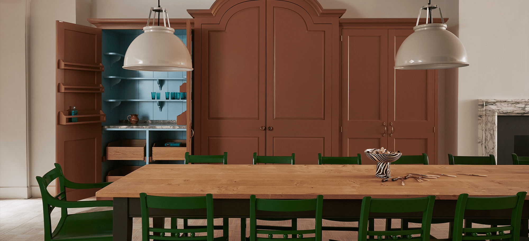  Custom designed larder with brown doors behind a long wooden table.