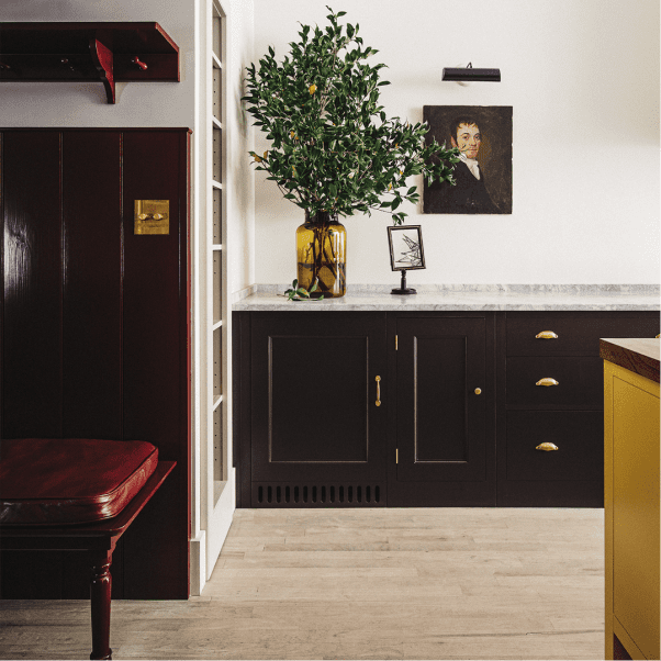 Bespoke cabinetry by Plain English featuring dark wood cabinets with brass handles, a marble countertop, and a custom yellow island.