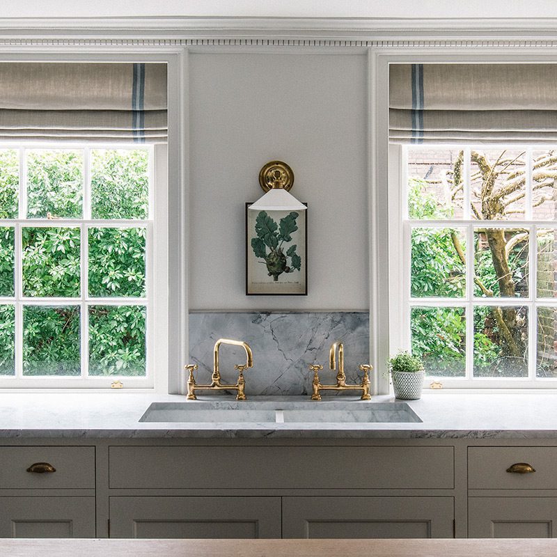 Interior view of the Walled Garden House kitchen, with bespoke cabinetry in a dark wood finish, large windows providing natural light, and custom brass accents throughout the space.