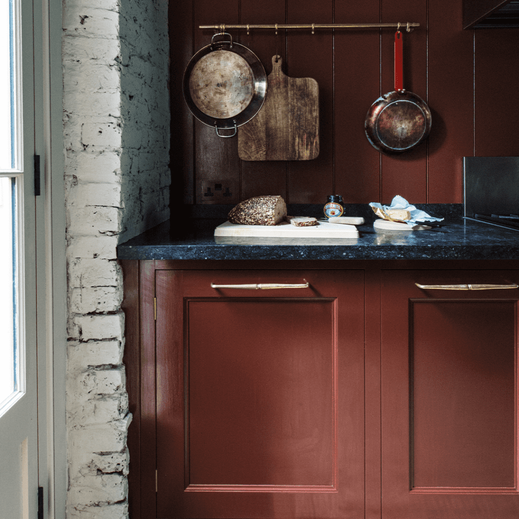 Bespoke cabinetry in rich red with brass handles, black countertop, and hanging kitchenware.