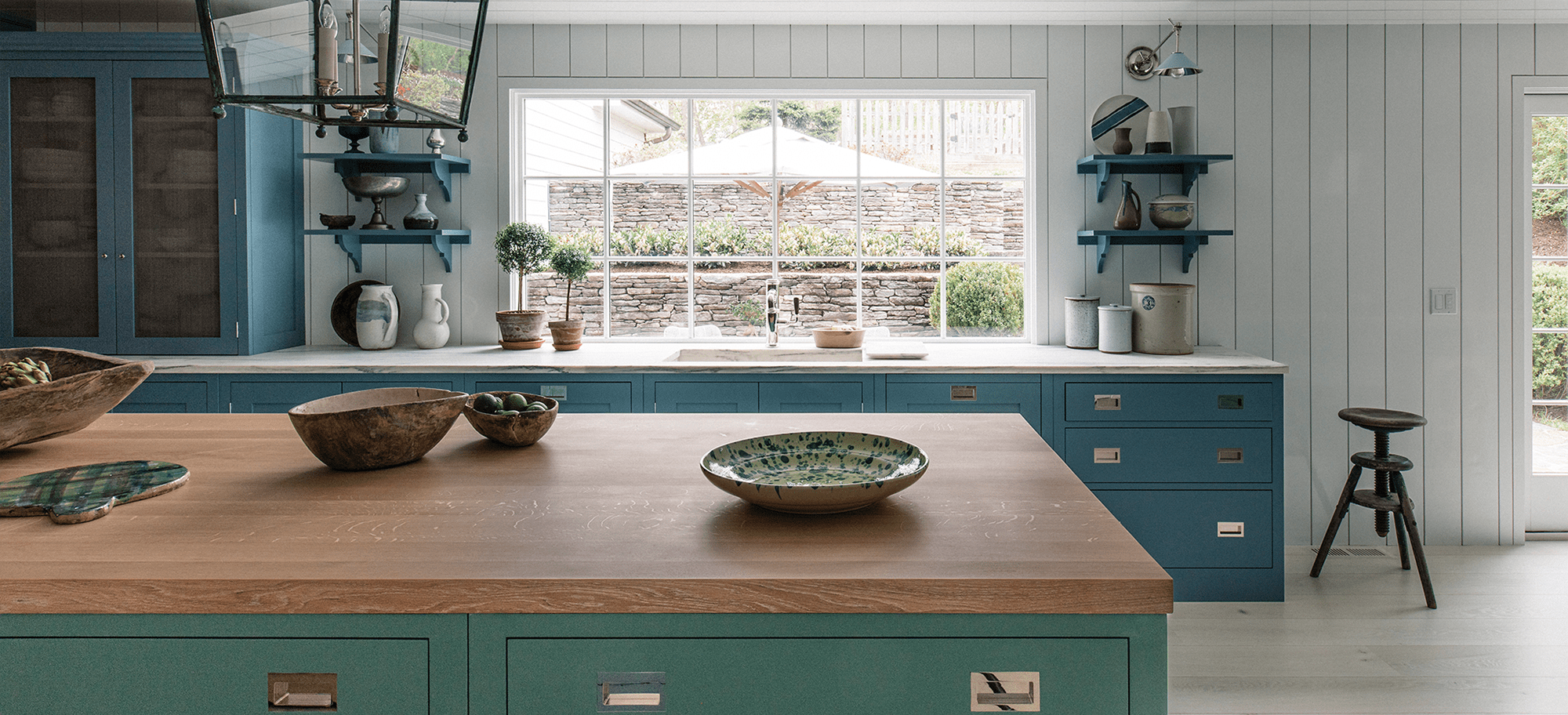  Bespoke cabinets in teal and turquoise with custom wooden countertops, featuring elegant shelving and unique hardware.