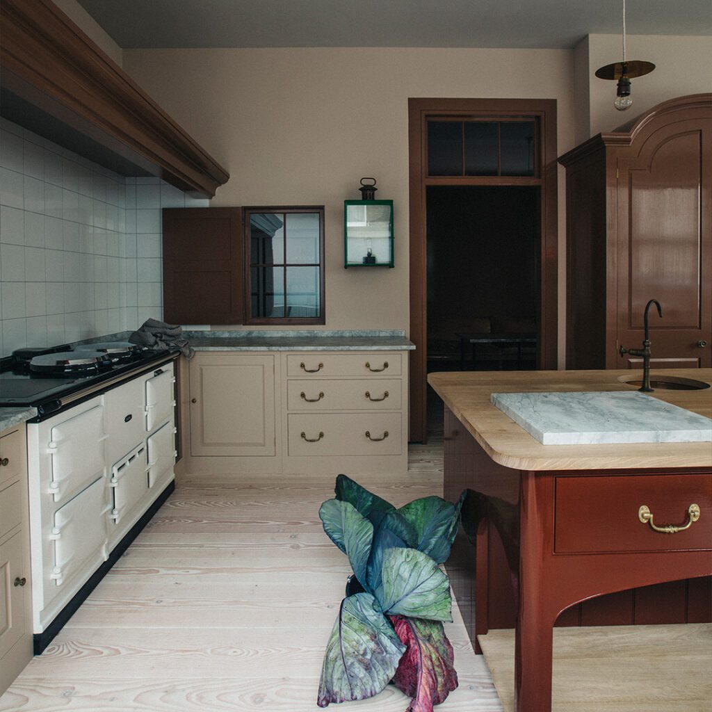 Kitchen with bespoke cabinetry in cream and marble countertops, featuring a classic stove and brass fixtures.