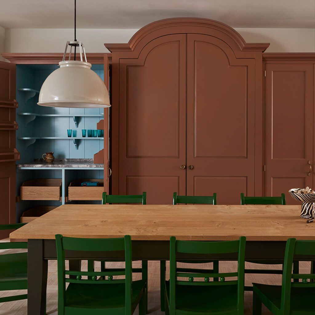 Bespoke cabinetry in warm brown with arched design, open shelving in blue, and a wooden table with green chairs.