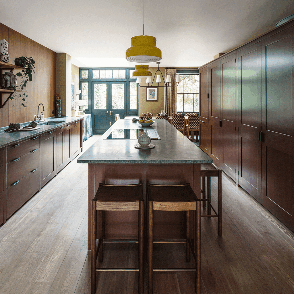 Bespoke cabinetry in rich brown with a large kitchen island, green marble countertop, and wooden stools.