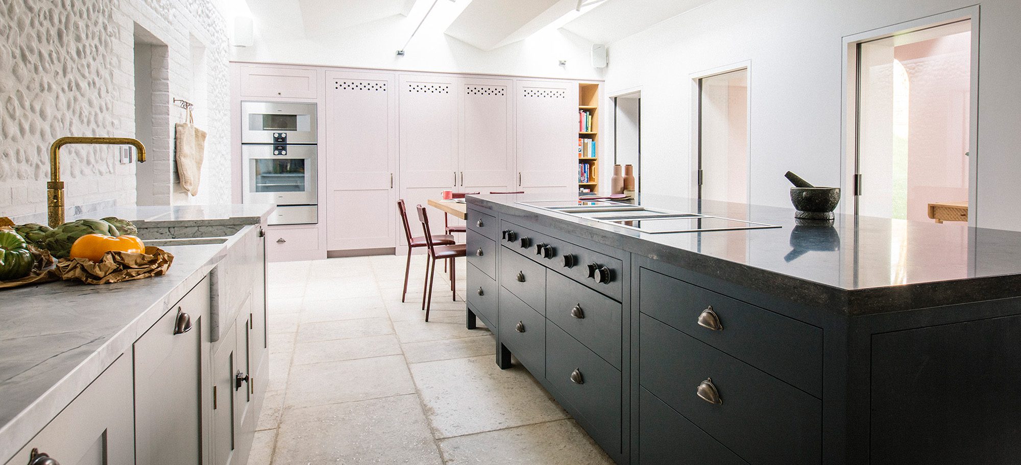  Custom kitchen featuring bespoke cabinetry by Plain English with a large island, dark countertop, and brass fixtures.