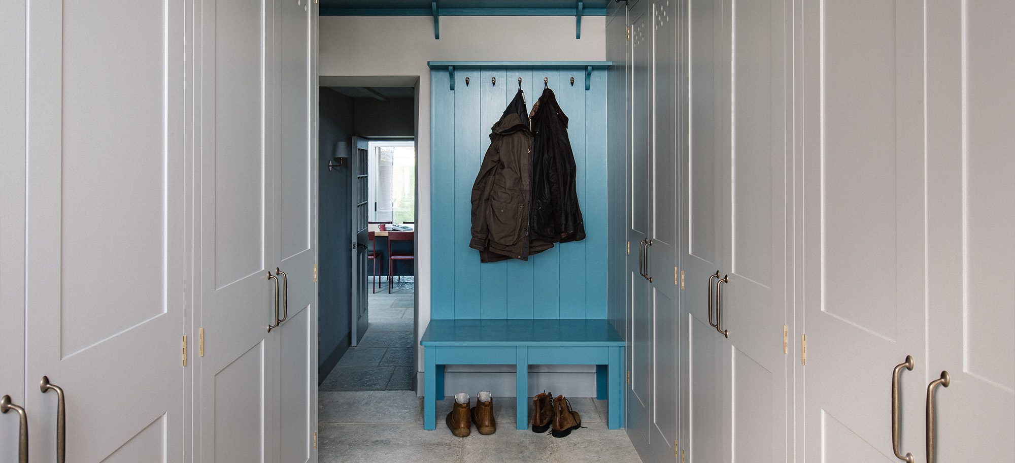  Bespoke cabinets in soft gray with brass handles, featuring a custom blue coat rack and bench.