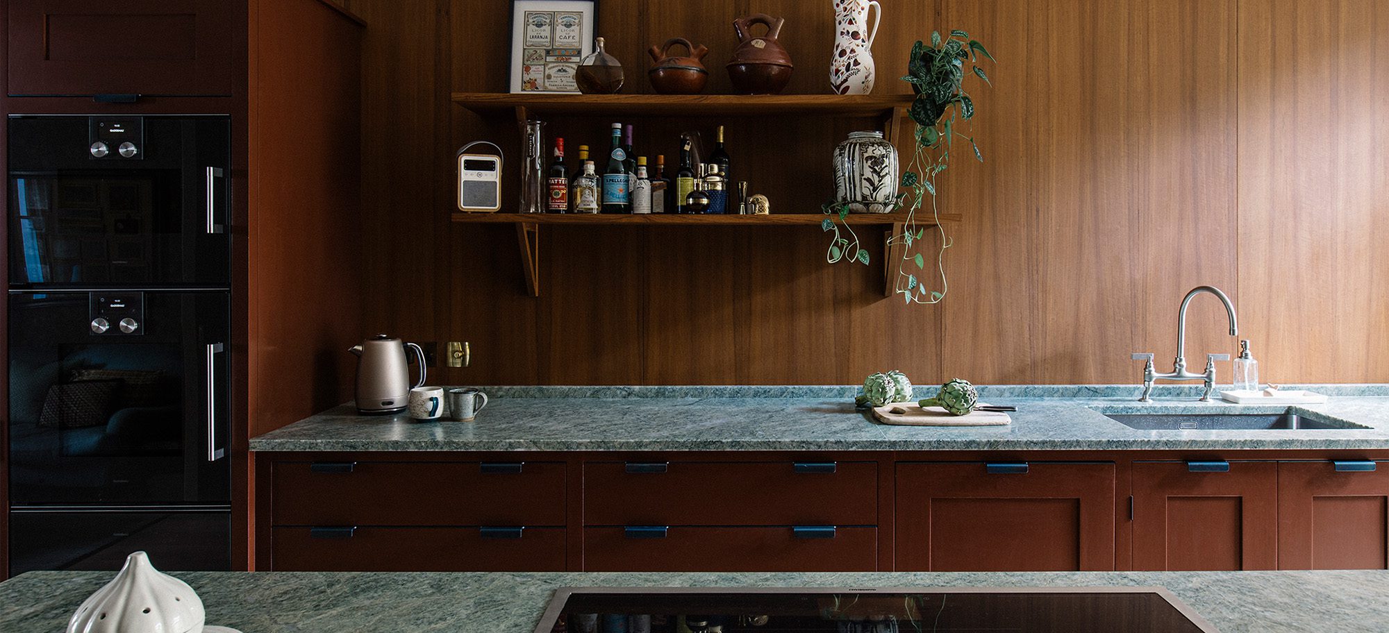  Bespoke kitchen cabinetry in rich brown with blue handles, featuring a custom green marble countertop and integrated appliances.