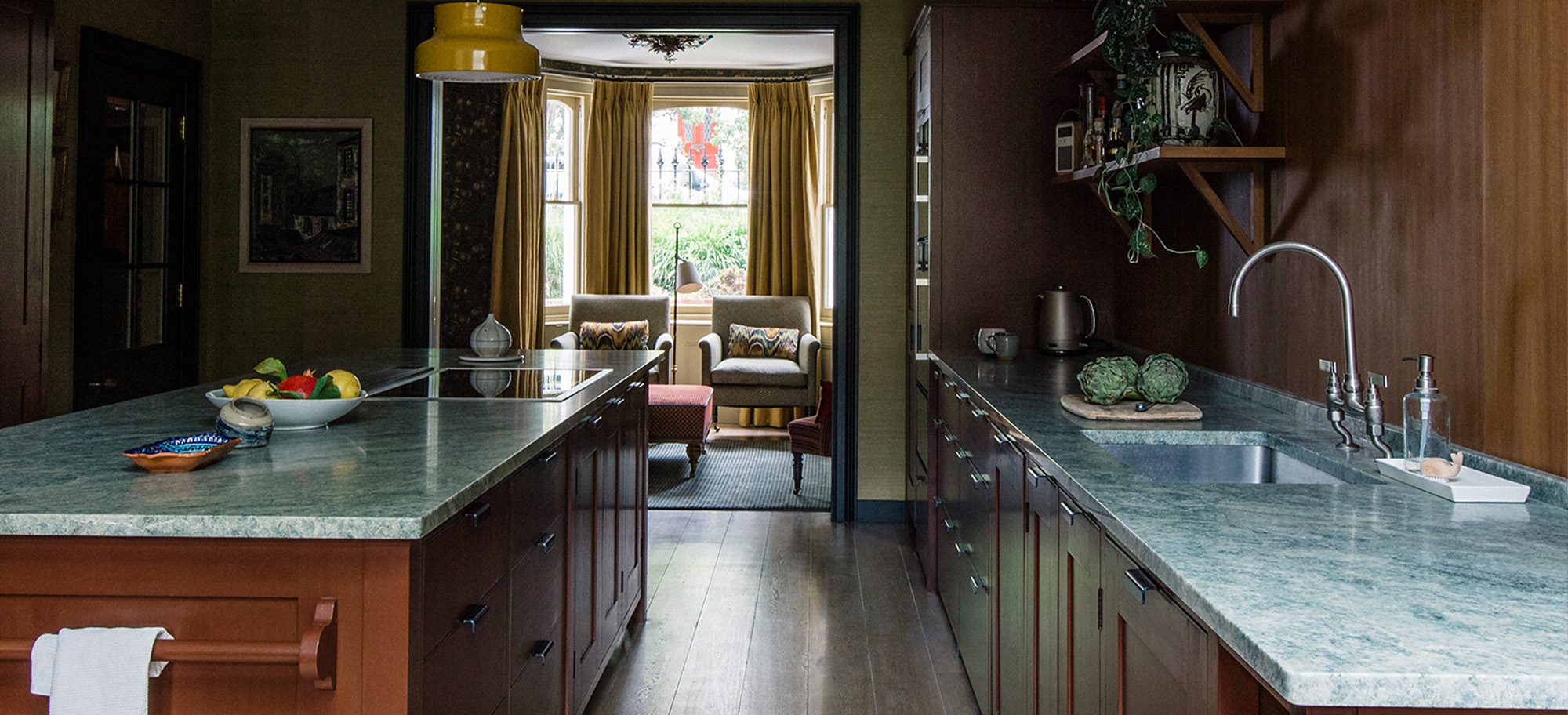  Kitchen with bespoke cabinetry in rich brown with custom green marble countertops, featuring a large island.