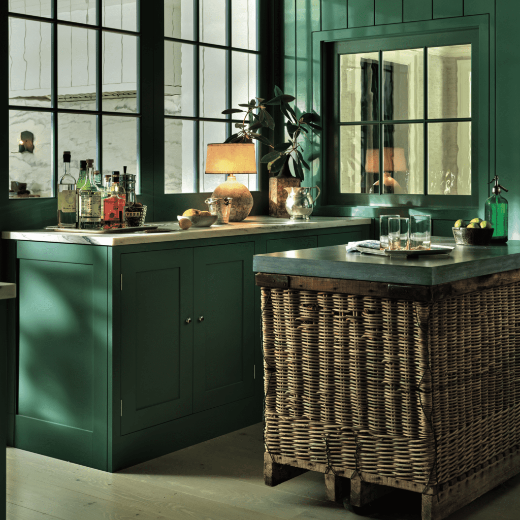 Bespoke green cabinetry with custom wicker island, featuring elegant countertops and stylish accessories.