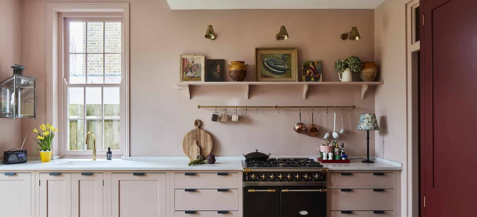  a kitchen with comtemporty and classic elements in a soft, warm pink and bespoke cabinetry with a black range cooker as a focal point.
