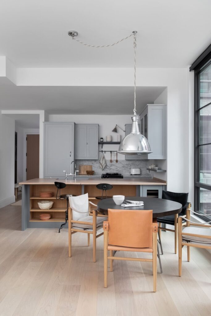 a kitchen and dining area featuring a simple, classic British aesthetic with light gray cabinets, a marble backsplash, and large central island with a tan countertop