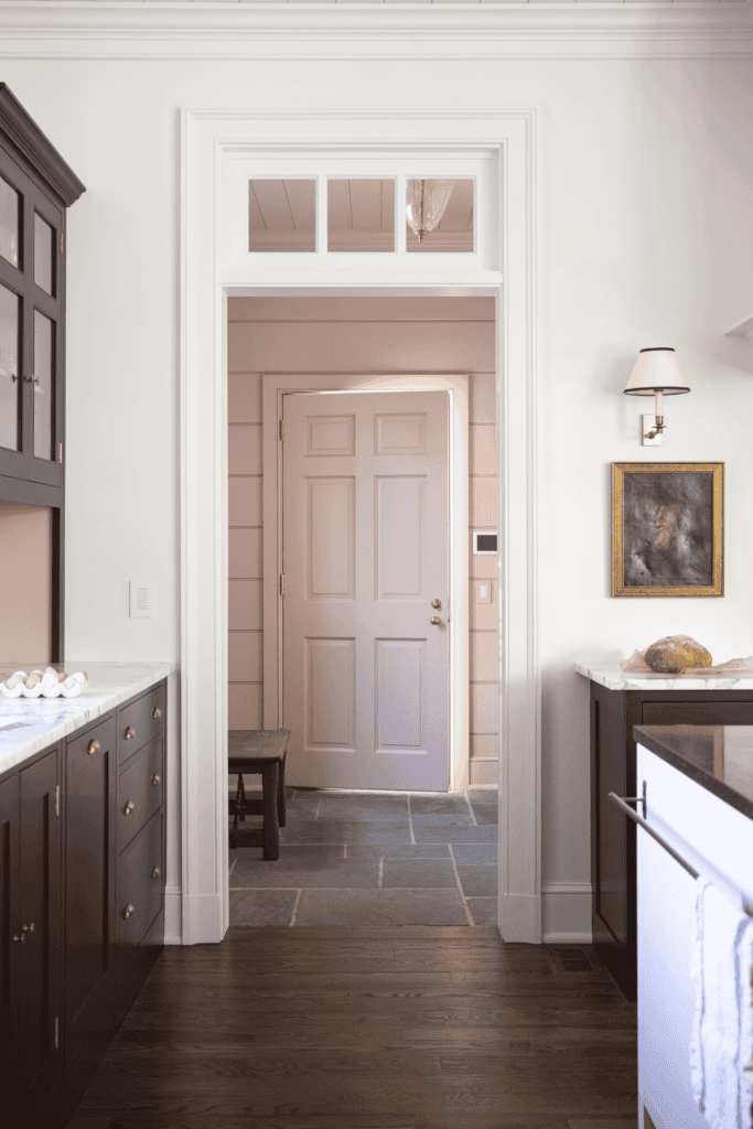 a traditional English kitchen and entryway featuring dark wood flooring, lighter off-white walls, and a stone-tiled entryway floor