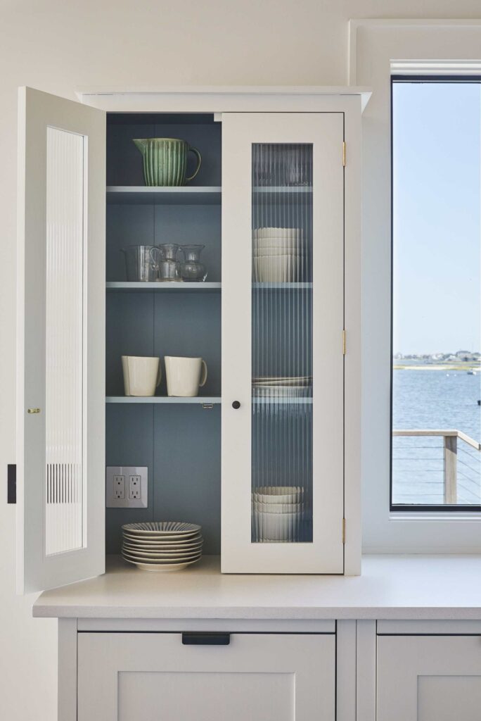 a contemporary built-in kitchen cabinet with white fluted glass doors and a light blue interior, featuring ample storage for dishes and mugs