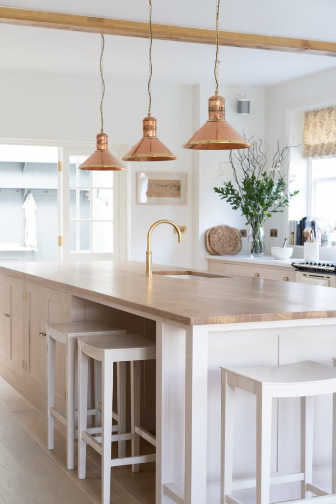 a kitchen painted in white with a large island with a light wood countertop with white, backless stools tucked underneath