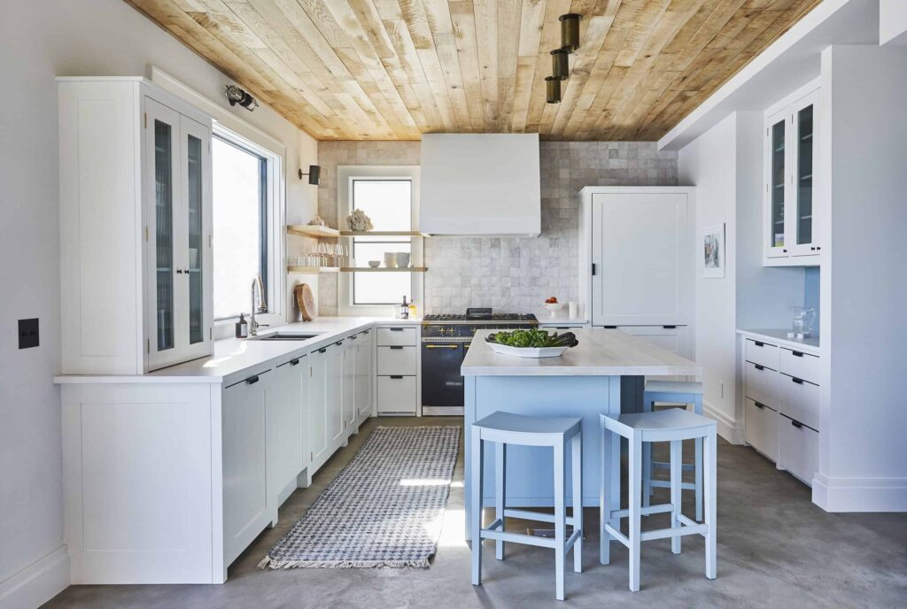 a kitchen in a Westhampton Beach house with a coastal vibe featuring custom white cabinetry, a light blue kitchen island with white countertops, and a wood plank ceiling