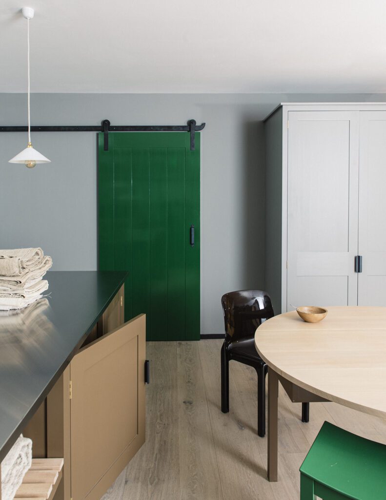 Kitchen door painted in pickle green, white cupboard, and taupe kitchen island opened slightly ajar