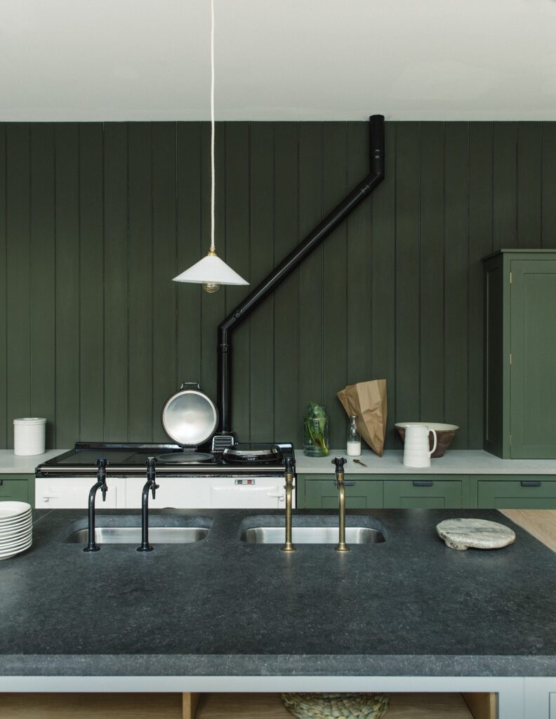 Army green painted kitchen paneling and cupboards with marbled counters, and dual faucet island