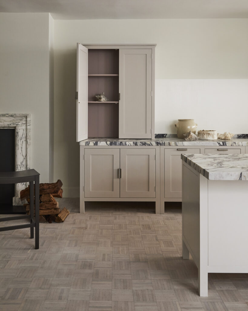 Beautiful marble counter tops in kitchen next to marble fireplace with beige cabinets, one of which has its doors open