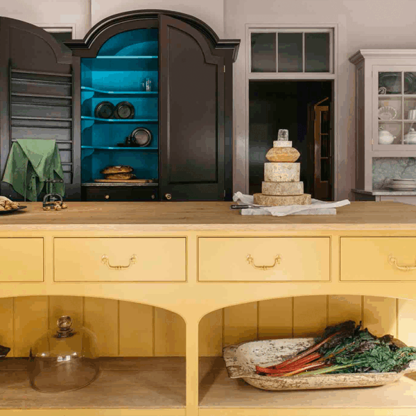 A kitchen with a yellow island, dark cabinetry with a blue interior, and a display of cheeses and vegetables.