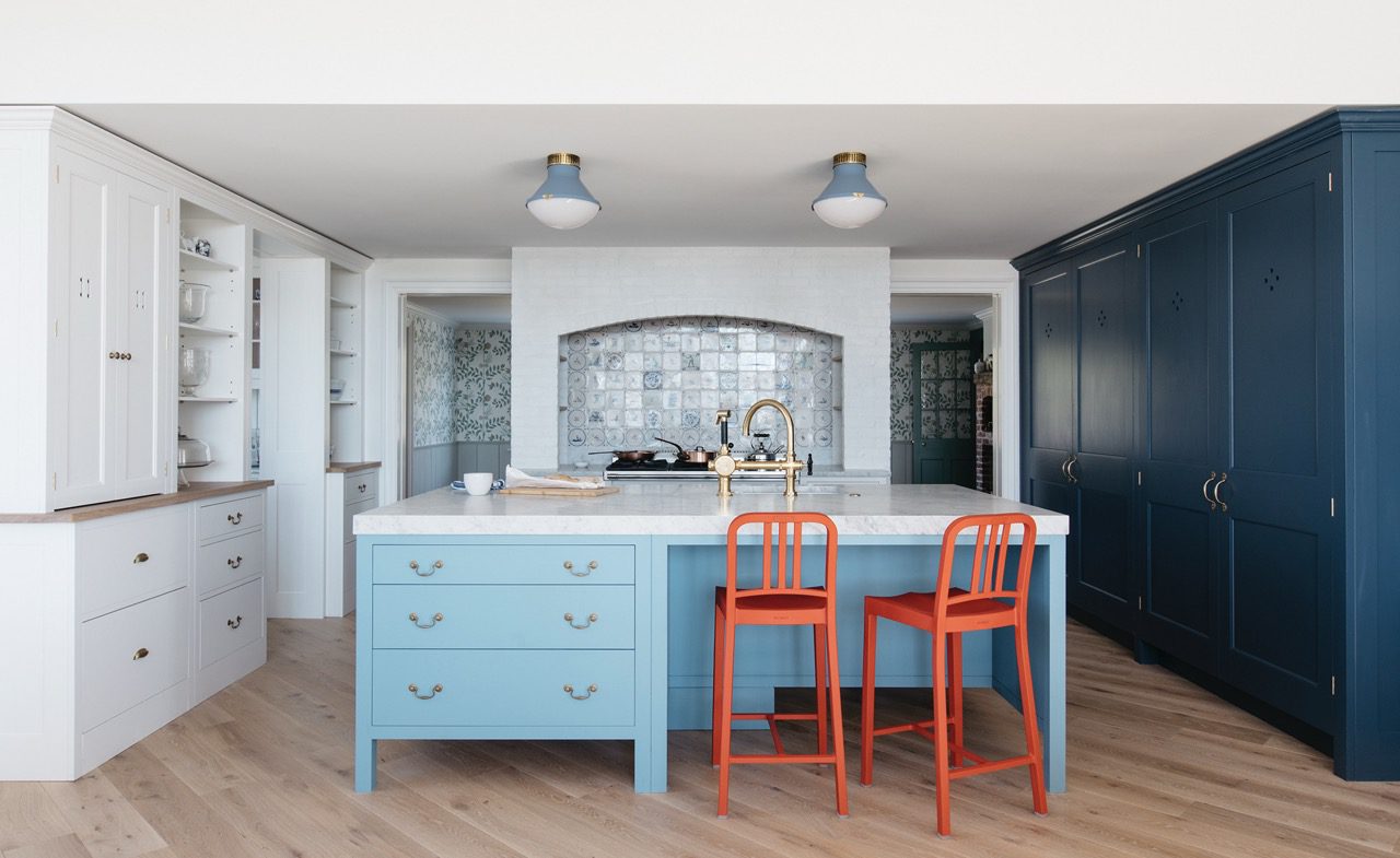  a bespoke kitchen with a light blue kitchen island, a marble countertop, and two bright orange bar stools