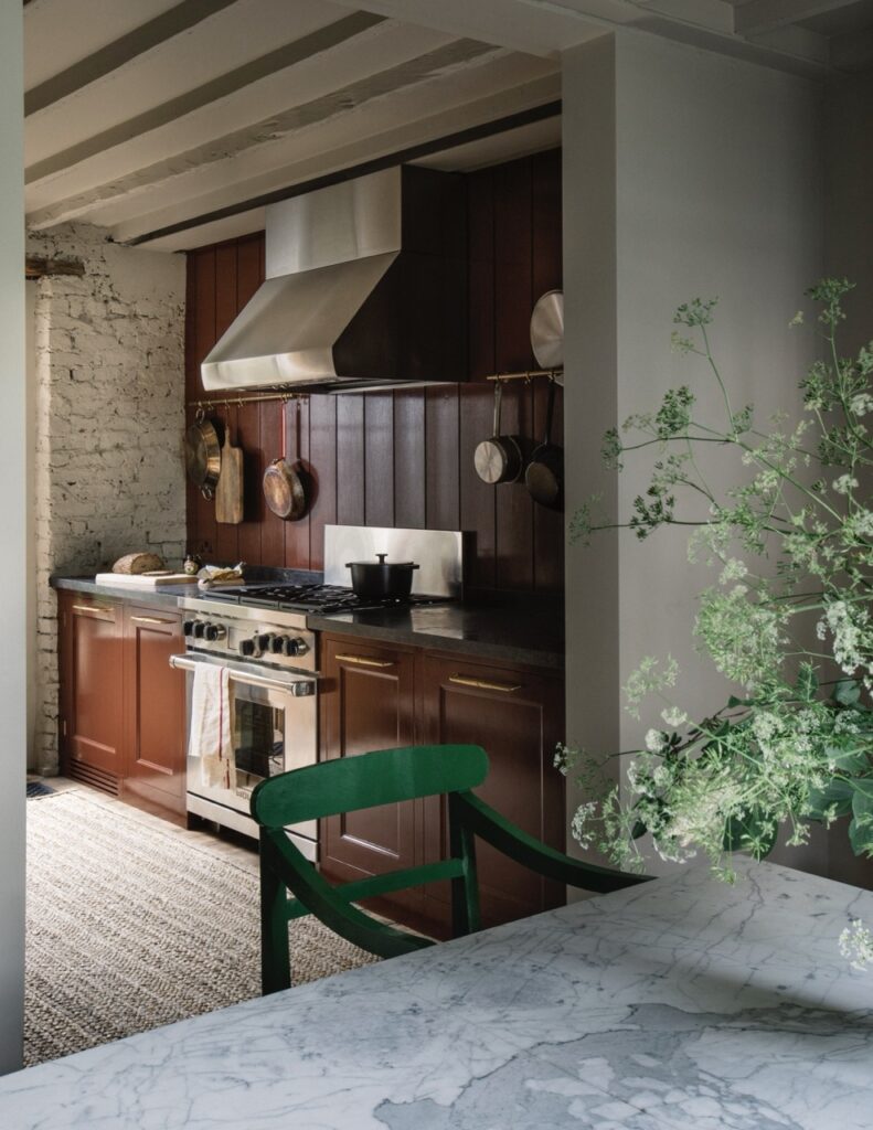 a kitchen featuring an oven with a large hood, rich, dark wood cabinetry with a marble countertop and a green chair