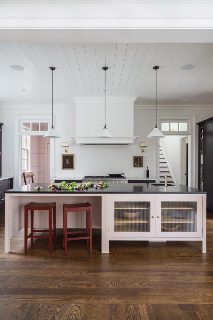 white kitchen with an island with white cabinets and red chairs