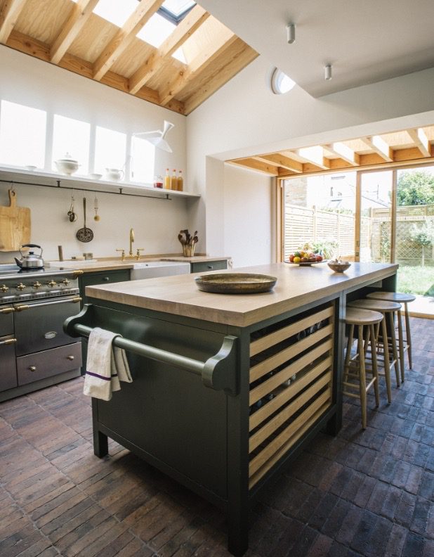 a well-lit comtemporary kitchen with bespoke, olive-green cabinetry and a large island with an oiled pippy oak worktop.