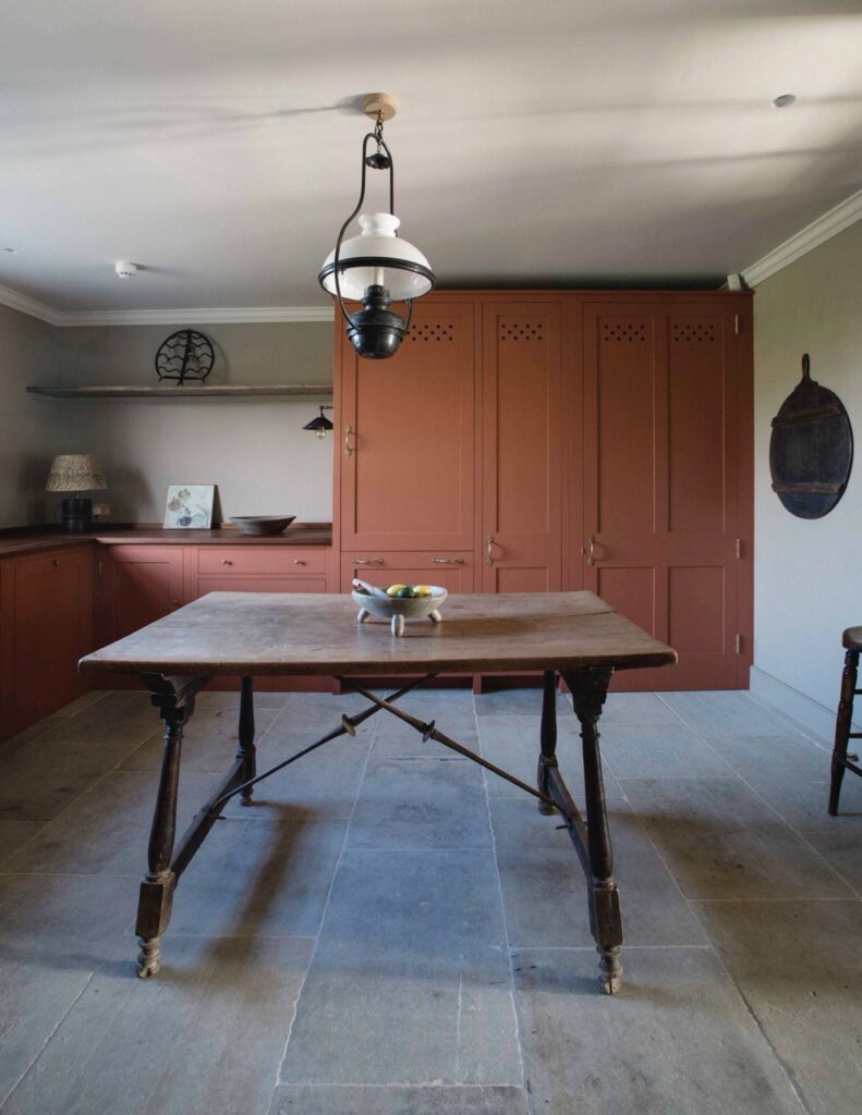 a pantry in a kitchen painted in a deep, chalky terracotta color with a large table in the middle of the kitchen
