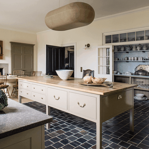 A spacious kitchen with a large wooden island, cream cabinetry, dark tiled floor, and a soft beige pendant light, featuring classic Georgian-inspired detailing.