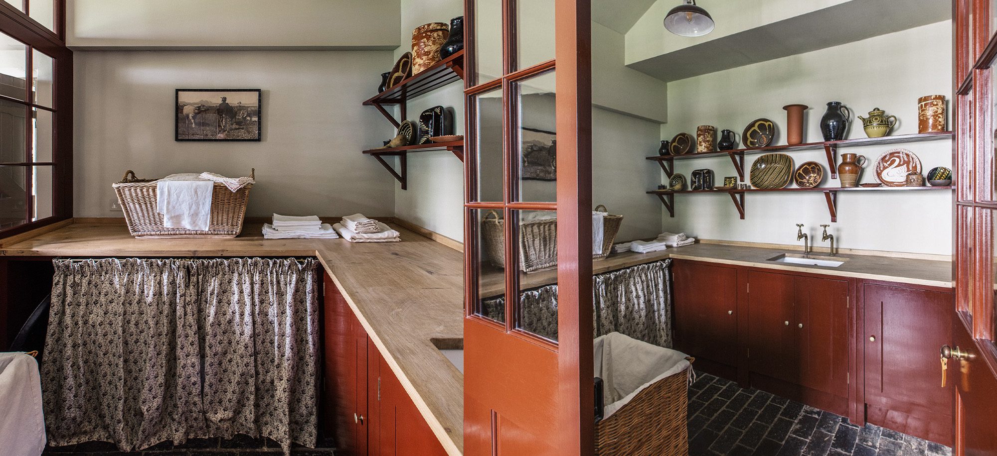  A rustic laundry room features rich red cabinetry, wooden countertops, and open shelves displaying pottery, with a wicker basket and folded linens adding a cozy touch.