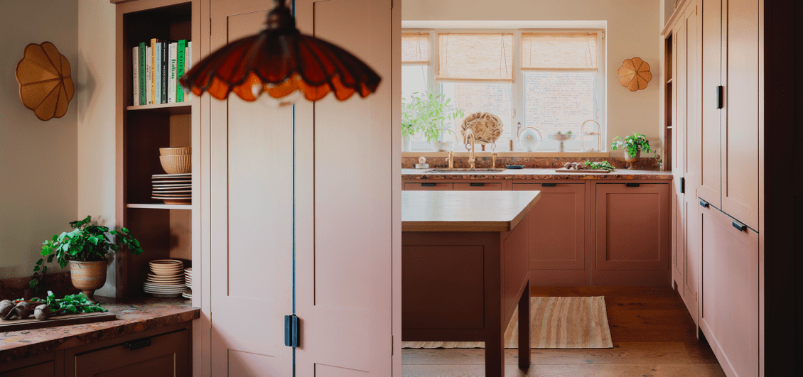  A warm kitchen with pink cabinetry, wooden floors, a central island, and a stained glass pendant light, featuring open shelving with books and dishes, and a window with woven blinds.