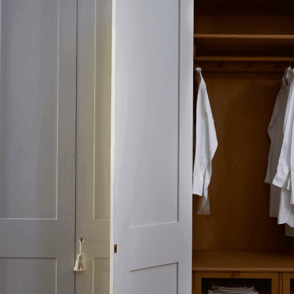 A partially open white wardrobe reveals neatly hung white shirts and wooden shelving inside.